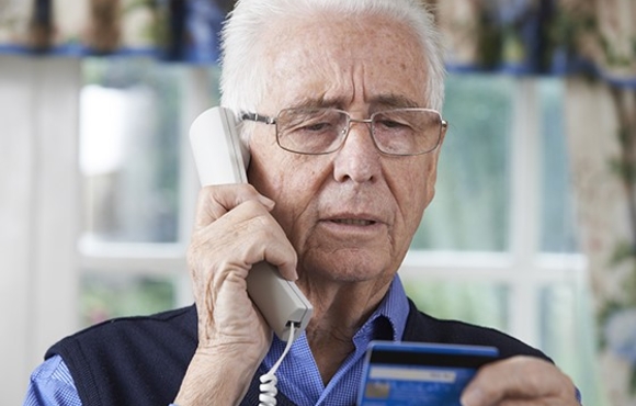 Older adult man on the phone holding a credit card.
