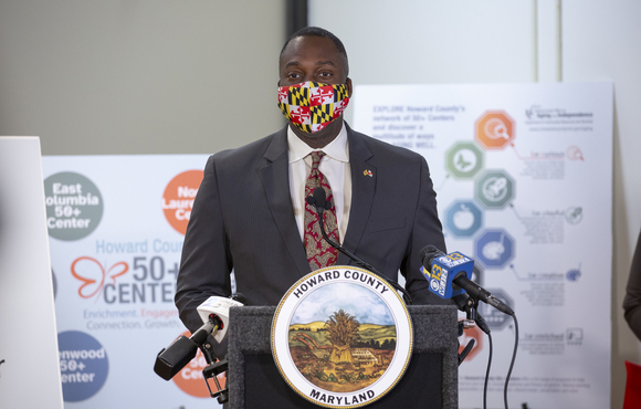 Calvin Ball at podium in front of 50+ center reopening boards