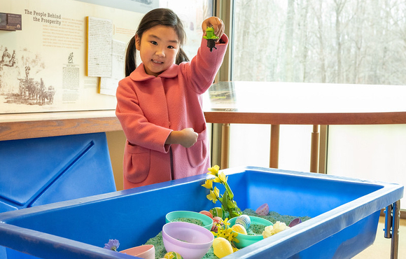 girl in pink coat holds up a toy