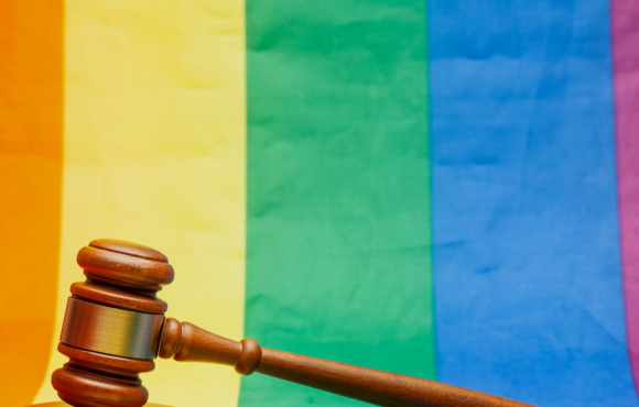 A wooden gavel resting on an LGBT Pride flag. 