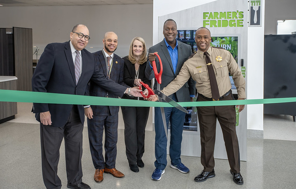 Image of Howard County Executive Calvin Ball and fellow local and state officials cutting a ribbon to mark the arrival of the Farmer's Fridge healthy vending machine to the Circuit Courthouse in Ellicott City.