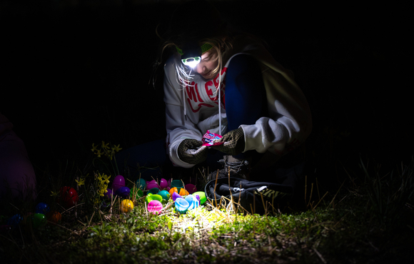 Teenager with flashlight lamp on head looking down and opening collected eggs. 