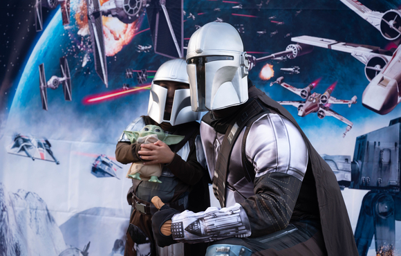 An adult dress in a Mandalorian costume posing for a photo with a child in same costume. 