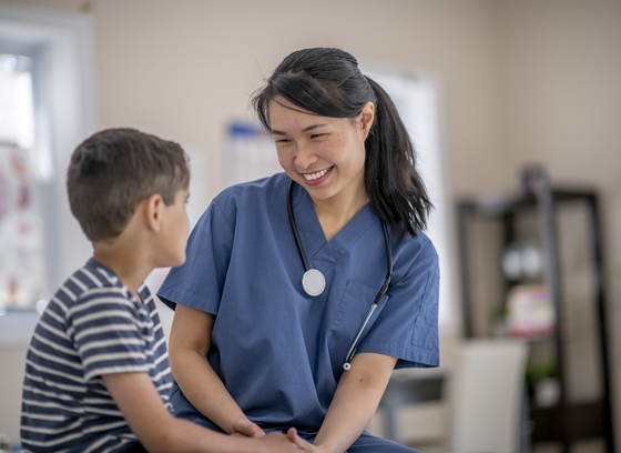Asian female nurse smiles at young caucasian boy patient