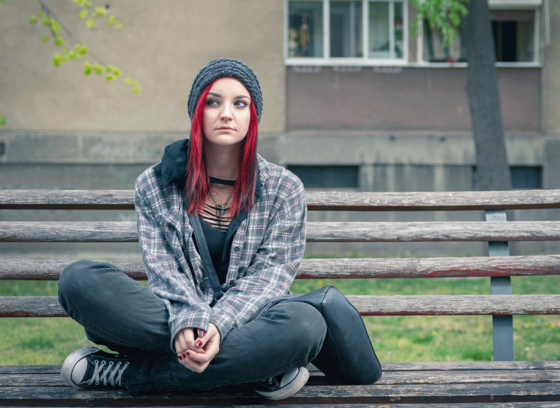 Image of a teen with red hair sitting on a bench, looking sad.