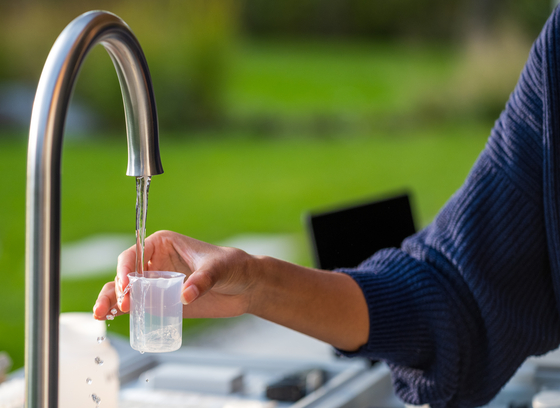 person holding test cup under running water faucet