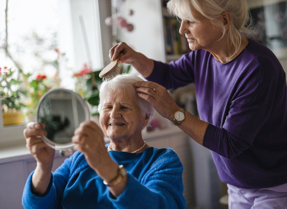 A person brushes an older adult's hair 