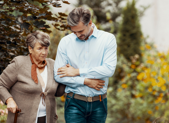 Caregiver helping older adult with walking stick 