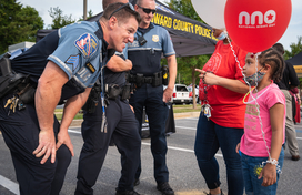 Uniformed officers interact with young girl holding a National Night Out Balloon