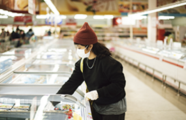 Woman buying frozen food in a supermarket, wearing a medical mask and gloves