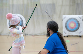 Young girl shooting bow and arrow with instructor