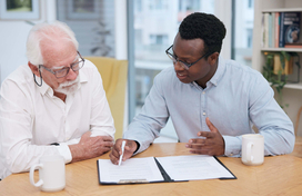 Older adult fills in paperwork with help from worker 