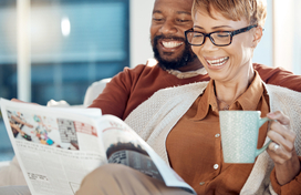 African American couple sitting on a soga drinking coffee and reading. 