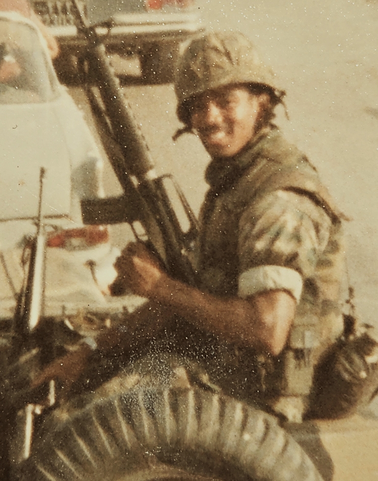 A photograph of Paul Rivers, holding a weapon and smiling at the camera