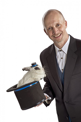 Magician Dave Thomen holding a top hat with a bunny coming out of it. 