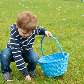 Image of a small boy picking up an easter egg in grass