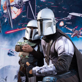 An adult dress in a Mandalorian costume posing for a photo with a child in same costume. 